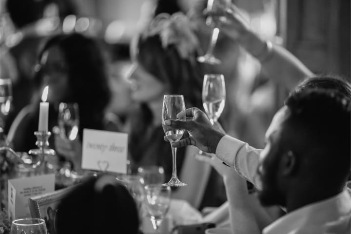 Black and white photo of wedding guests at a table raising a toast